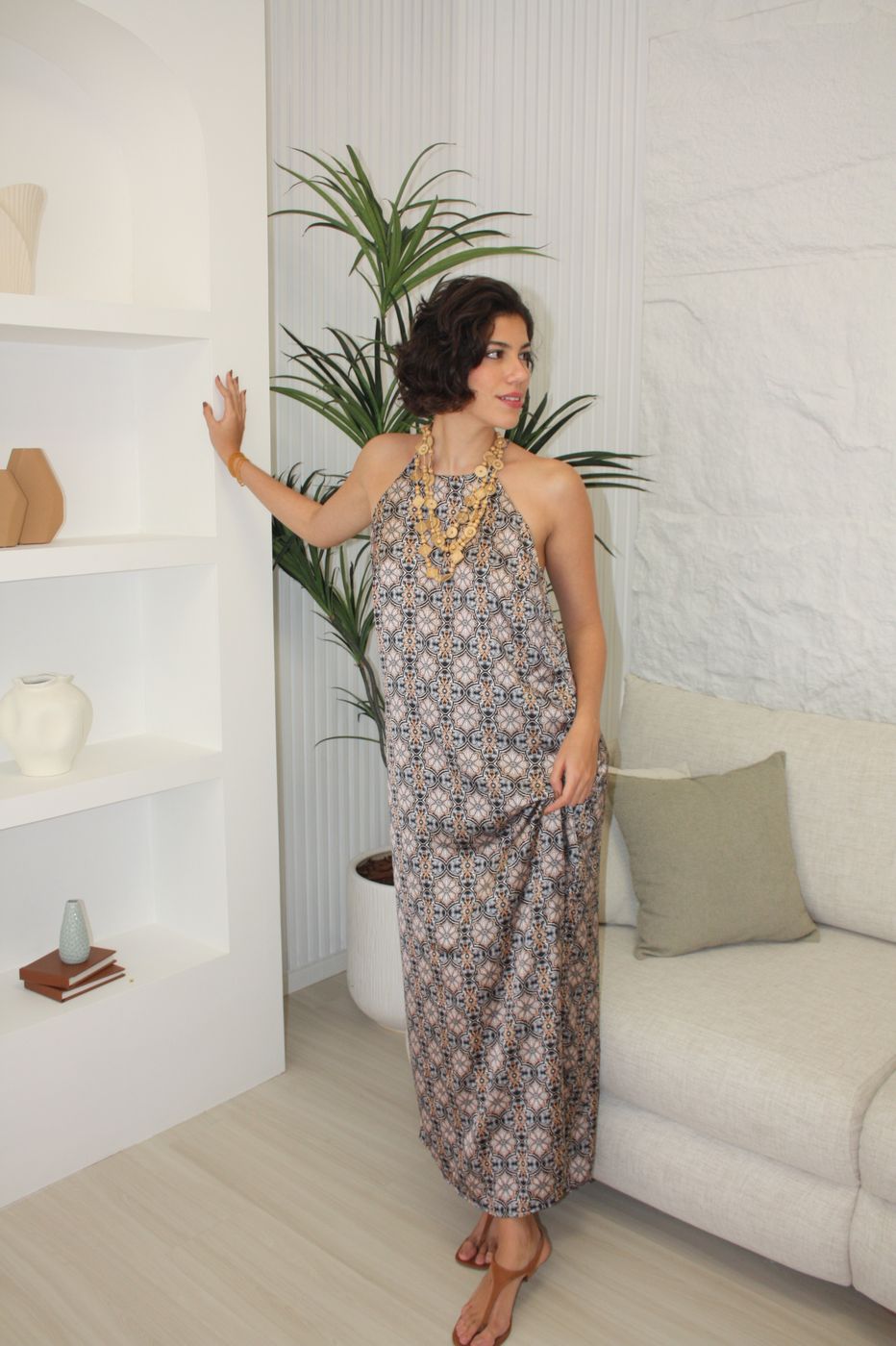 Fernanda Pontes em vestido estampado com colar artesanal, sentada em sofá claro