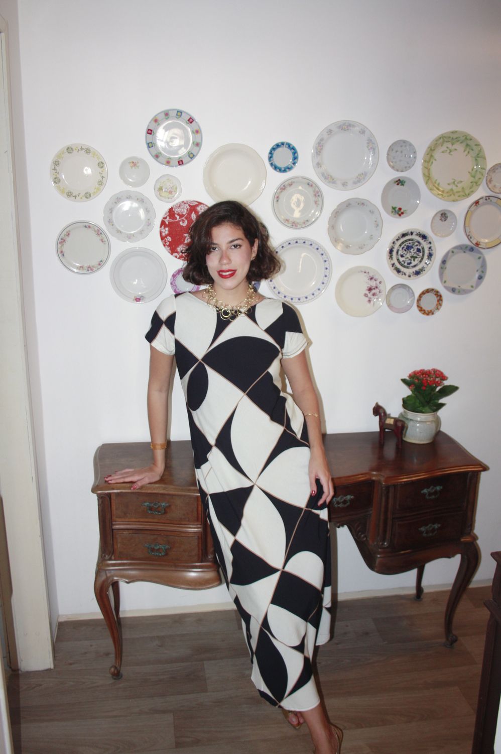 Fernanda Pontes em vestido gráfico preto e branco, em frente a parede decorada com pratos