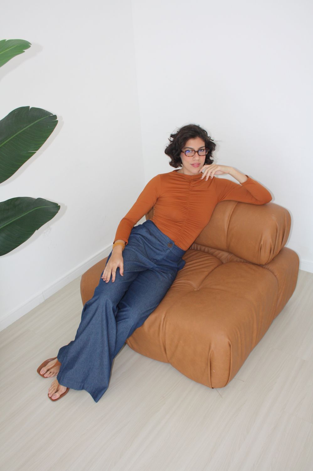 Fernanda Pontes em blusa terracota e calça jeans, sentada em poltrona de couro caramelo